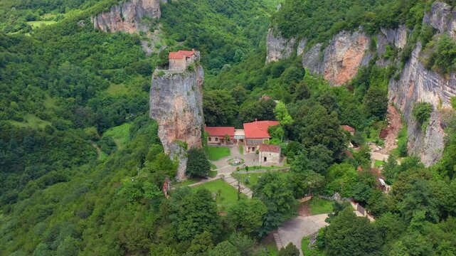 Katskhi monastery fills aerial view beneath the towering rock column and cliffside church, supporting pilgrimage tourism, Orthodox history, religious architecture and Georgian heritage media.