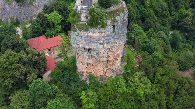 Katskhi Pillar rises in aerial view beside monastery roofs and dense woodland, supporting spiritual travel, Georgian Orthodoxy, landscape tourism and landmark documentary media production projects.