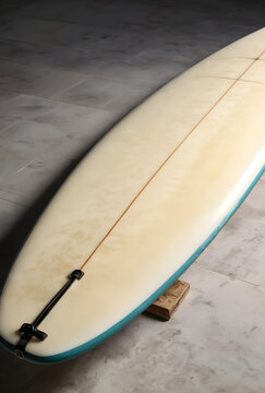 Vintage longboard surfboard with a teal rail and leash plug, resting on a wooden block on a concrete floor, surf culture and hobby