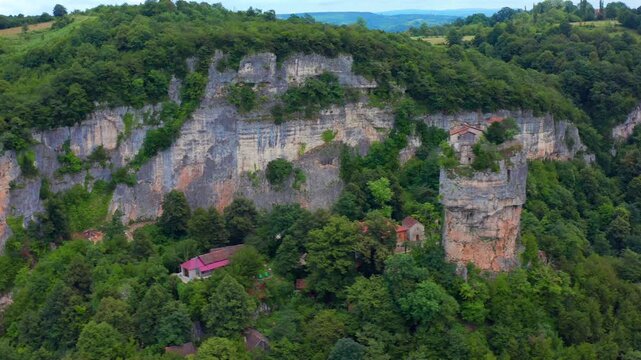 Aerial drone moves sideways past Katskhi Pillar in Georgia, framing the isolated rock column, summit church and wooded cliffs for religious tourism, geology education and destination promotion.