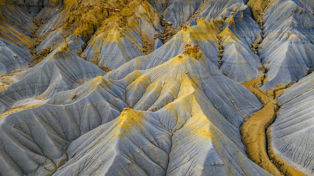 Aerial view of badlands with colorful eroded clay hills, intricate ridges, and dry drainage channels in Hanksville, Utah, United States.