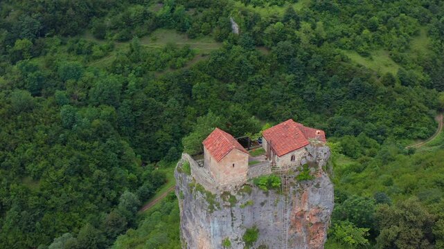 Aerial drone circles Katskhi Pillar in Georgia, revealing the summit monastery, limestone monolith and dense forest for pilgrimage tourism, sacred architecture and cultural heritage projects.