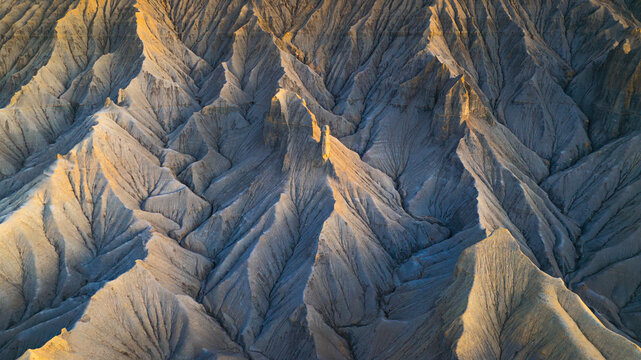 Aerial view of the eroded badlands landscape with sharp ridges and deep shadows cast by the golden hour light in Hanksville, Utah, United States.