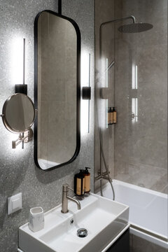 Contemporary bathroom design showcasing a white basin and faucet. A rectangular mirror flanked by vertical led lights. And a glass enclosed shower with a rain head