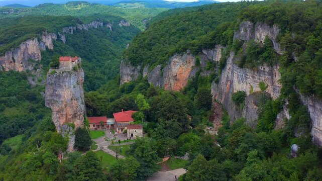 Katskhi Pillar dominates elevated aerial view above monastery roofs and limestone canyon in Imereti, supporting pilgrimage tourism, Georgian heritage, geology education and landmark promotion.