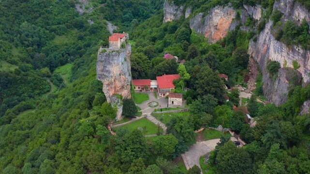 Aerial drone lands near Katskhi Pillar in Georgia, approaching the forest monastery and towering limestone monolith for religious tourism, spiritual retreats, geology media and travel promotion.