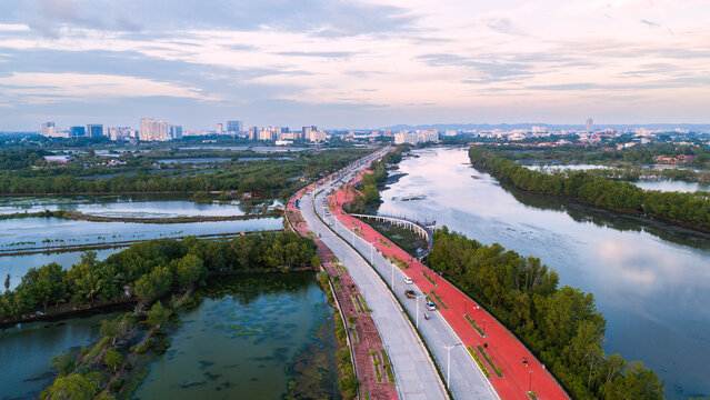 Iloilo City, Philippines - 18 July 2026: Aerial view of Iloilo Sunset Boulevard with its red path, lush mangroves, and fish ponds, with the city skyline in the background.