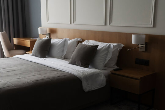 Clean and inviting bed with crisp white and grey pillows, a cozy duvet, and wooden furniture, creating a comfortable and elegant atmosphere in a contemporary hotel room