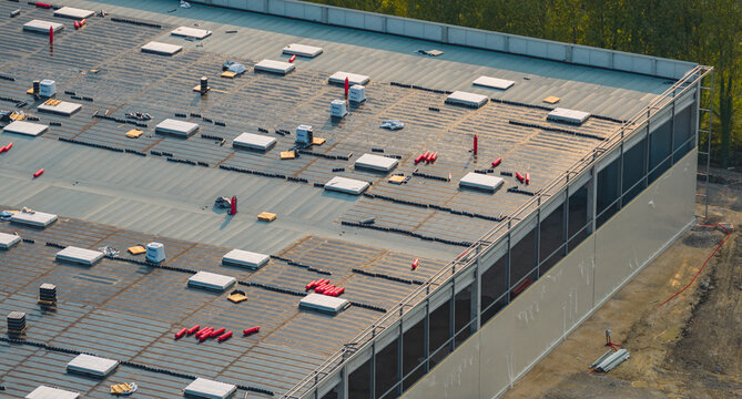 Loriol-sur-Drome, Auvergne-Rhone-Alpes, France - 26 July 2026: Aerial view of a modern industrial warehouse under construction, featuring roofing works, skylights, and insulation materials.