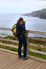Obraz premium Woman tourist takes photos of Slieve League cliff landscape in County Donegal, Ireland. Viewpoint terrace.