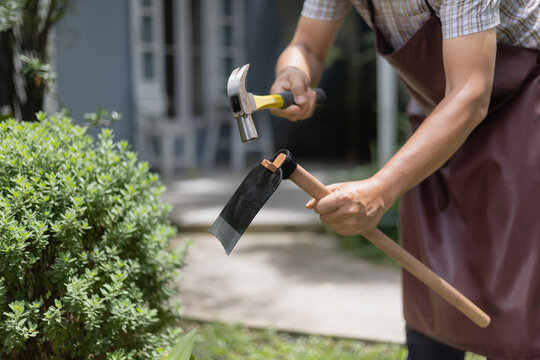 A Man Fixing a Loose Hoe Handle by Driving a New Wooden Wedge