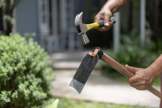 Retired Asian Man Fixing a Loose Hoe Handle by Driving a New Wooden Wedge