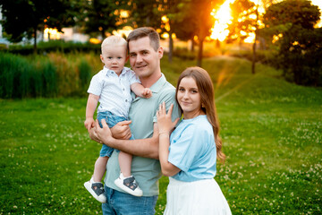 Fototapeta premium parents, mom, dad, and a small child are walking on a green lawn in the summer, having fun together, hugging, and playing outside in the summer. A happy family