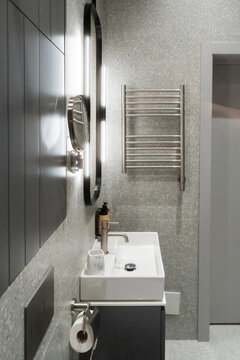 Contemporary bathroom presenting a sleek wall mounted sink with modern faucet, an oval illuminated mirror, and a wall mounted towel warmer, accentuating minimalist design and comfort