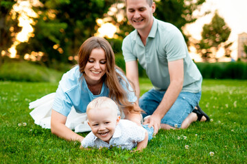 Fototapeta premium parents, mom, dad, and a small child are walking on a green lawn in the summer, having fun together, hugging, and playing outside in the summer. A happy family