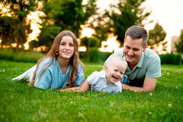 Fototapeta premium parents, mom, dad, and a small child are walking on a green lawn in the summer, having fun together, hugging, and playing outside in the summer. A happy family