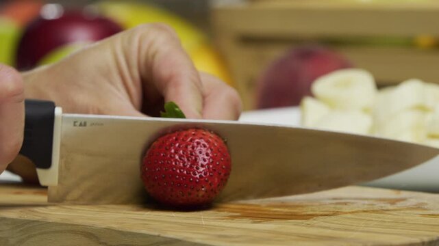 Sharp knife slicing through delicious strawberry on cutting board in slow motion