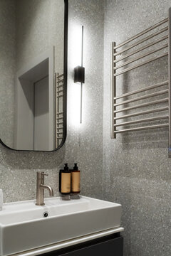 Contemporary bathroom space showcasing a stylish sink cabinet, sleek mirror with an integrated light fixture, a brushed steel faucet, and a towel warmer on a textured terrazzo wall