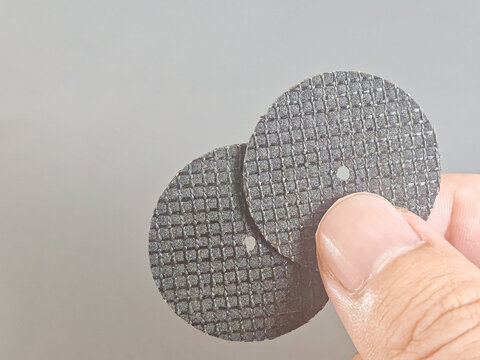 industrial abrasive cutting discs held by a hand, showing textured grinding wheel surfaces and manufacturing materials. Suitable for industrial tools, engineering, construction equipment, workshop