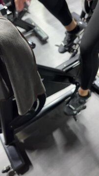 Woman riding spin bike in gym with focus on legs and pedals