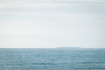 Fototapeta premium Distant silhouette of the Berlengas islands on the horizon of the blue Atlantic Ocean. Photographed from Santa Cruz, Portugal, featuring vast sky copy space for design