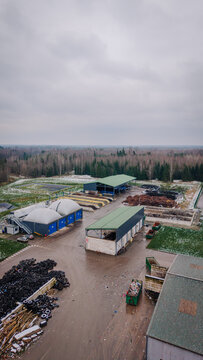 Valmiera, Latvija - 21 November 2025: Aerial view of a waste management and recycling facility with industrial buildings, piles of tires, and compost areas surrounded by forest.