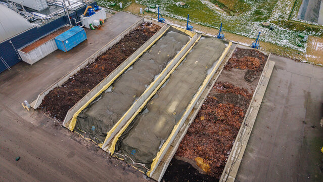 Valmiera, Latvija - 21 November 2025: Aerial view of a waste management and recycling facility with large composting bays covered by tarps and piles of organic waste in an industrial site.