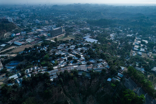 Chittagong, Bangladesh - 10 March 2022: Aerial view of dense housing on hilly terrain, showing small metal-roofed homes, trees, and steep slopes prone to landslides.