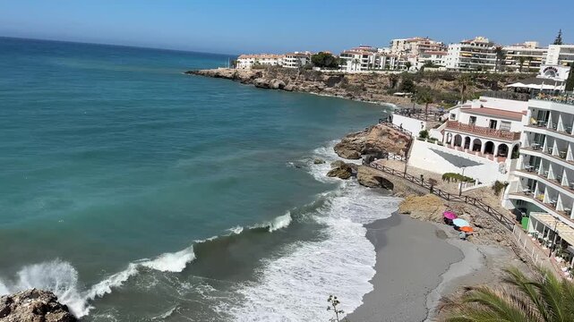 Static panoramic view of Nerja on Spain's Costa del Sol, featuring whitewashed buildings, the Mediterranean coastline and crystal-clear waters in daylight.