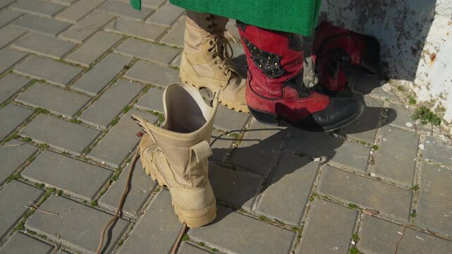 Boots footwear changing person replaces red decorative boots with tan tactical combat boots on a sunny paved sidewalk outdoors