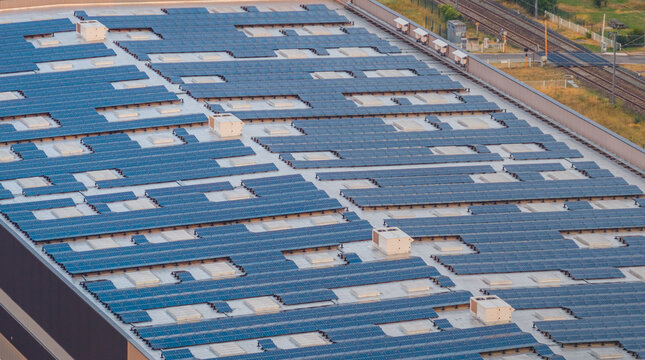 Alixan, France - 25 July 2026: Aerial view of a modern industrial warehouse roof covered with photovoltaic solar panels, featuring adjacent railway lines and industrial infrastructure.