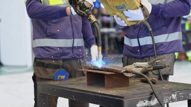 Industrial worker operating welding equipment with sparks and bright light in manufacturing environment