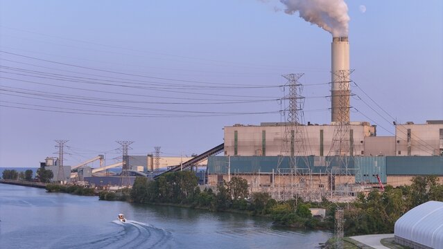 Monroe, Michigan, United States - 25 July 2026: Aerial view of DTE Energy Monroe Power Plant with smoke rising from the chimney, power lines, and a small boat on the river.