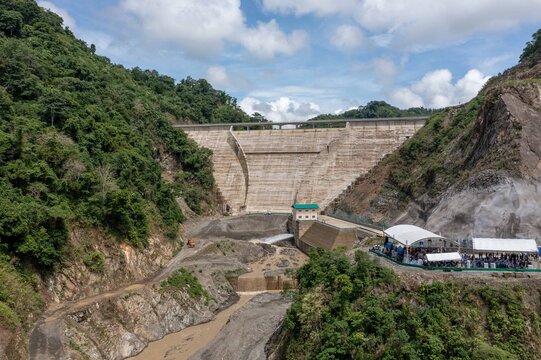 Calinog, Philippines - 16 July 2024: Aerial view of the Jalaur Reservoir Dam surrounded by lush mountains, featuring the concrete structure, riverbed, and a white event tent.