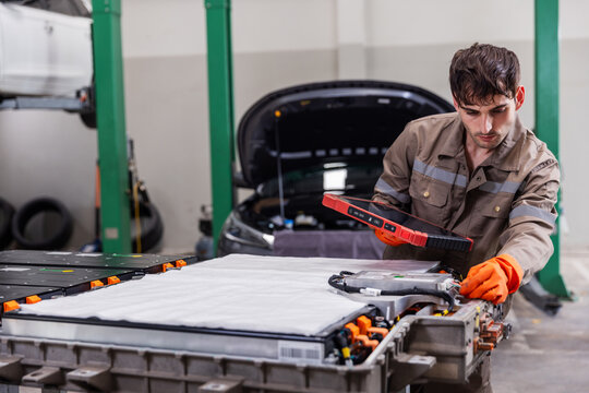 Skilled electric vehicle technician inspecting a high-voltage battery pack using a professional digital diagnostic tablet in a modern EV service workshop.