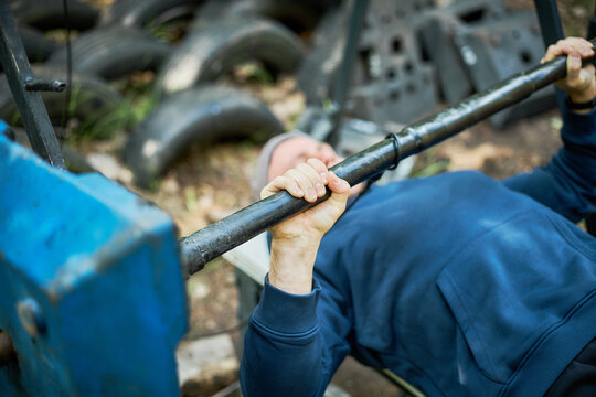 Close up of young adult man lifting barbell on outdoor bench, training upper body strength and fitness endurance. Ideal for gym promotion, workout programs, healthy lifestyle marketing