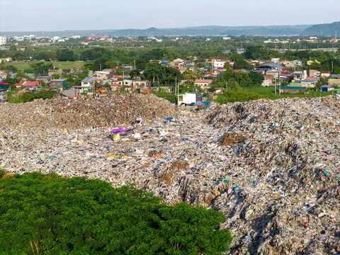 Iloilo City, Philippines - 25 July 2026: Aerial view of the Iloilo City Landfill, showing large piles of waste, surrounding residential buildings, trees, and distant hills.