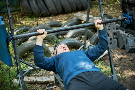 Young adult Caucasian man lifting barbell on improvised outdoor bench, training strength and endurance in rugged setting. Useful for fitness motivation, resilience, workout content