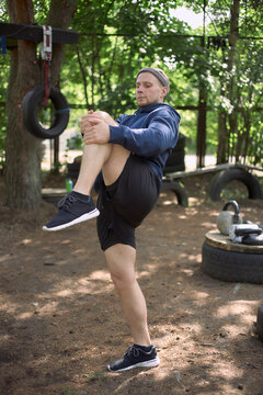 Vertical shot of young adult Caucasian man stretching knee during outdoor workout, improving mobility and balance. Fitness marketing, personal training, wellness campaign use