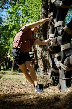 Vertical shot of young adult man climbing outdoor obstacle wall during fitness training, building strength and endurance. Useful for wellness campaigns, boot camp promotion