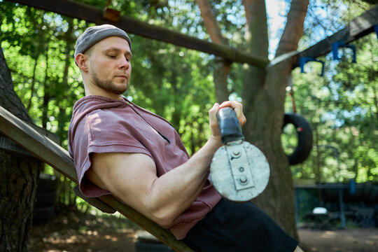 Young adult Caucasian man exercising with kettlebell on incline bench in outdoor gym, building strength and fitness. Useful for workout training, healthy lifestyle, wellness marketing