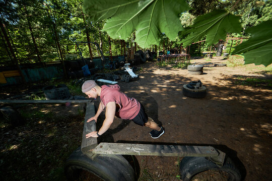 Young adult Caucasian man exercising on outdoor obstacle course, performing incline push ups for strength training and endurance. Useful for fitness boot camp or wellness marketing