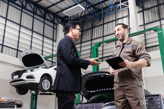 Professional EV technician reviewing repair results with a customer during an electric vehicle service handover in a modern automotive workshop.