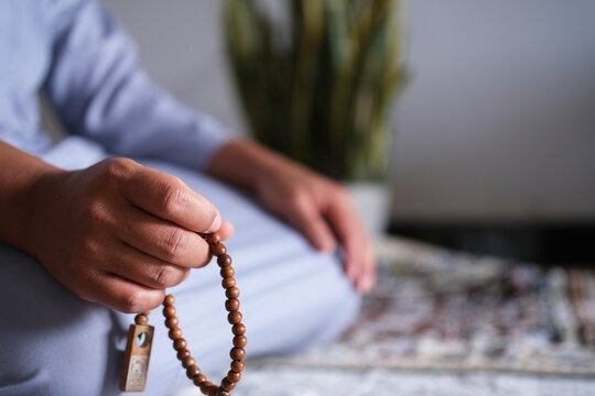 Close-up of hands reciting dhikr using prayer beads against a blurred background. Hands reciting dhikr. A man reciting dhikr while holding a prayer beads. A Muslim's worship activity.
