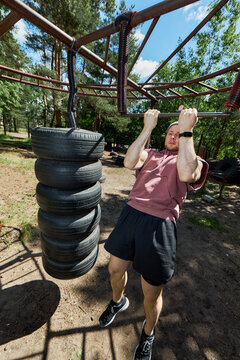 Vertical shot of young adult Caucasian man doing pull ups on outdoor obstacle course, training upper body strength and endurance. Fitness marketing, boot camp promotion, active lifestyle