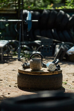 Vertical shot of kettlebell and boxing gloves resting on tire platform in outdoor gym, suggesting functional training and fitness routine. Useful for workout promotion and wellness marketing