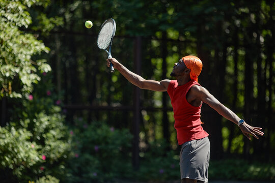 Black young adult man serving tennis ball on outdoor court, training for fitness and competitive sport. Image supporting active lifestyle, wellness, recreation, sports marketing