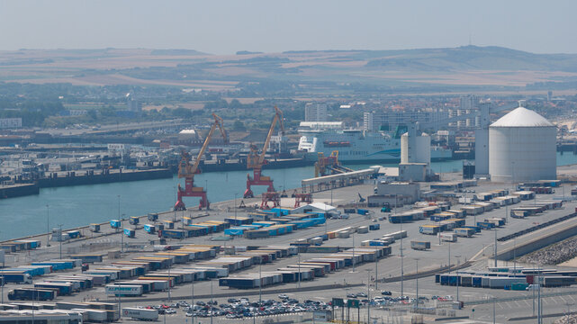 Calais, France - 09 July 2026: Aerial view of the Port of Calais ferry entrance with cargo cranes, parked semi-trailers, and a ferry docked in the harbor.