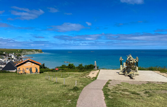Arromanches in Normandy, France: World War II D-Day overlook with a German 88mm Flak gun, Mulberry B artificial harbor mural and historic concrete caissons ruins in the Atlantic Ocean.
