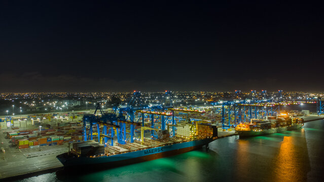 Accra, Ghana - 25 July 2021: Aerial view of MPS Terminal 3 at night with large container ships, gantry cranes, and stacks of shipping containers illuminated under the night sky.